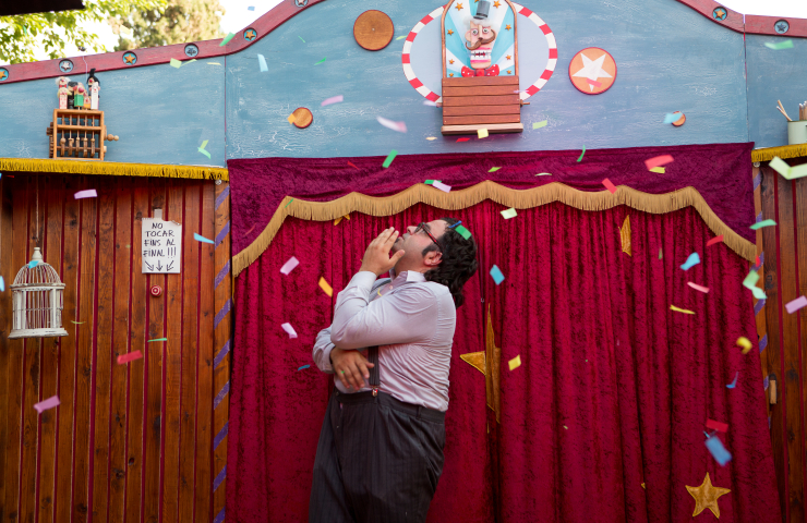 Escenario de títeres con confeti, mientras un hombre observa, mirando hacia arriba, cómo cae sobre él